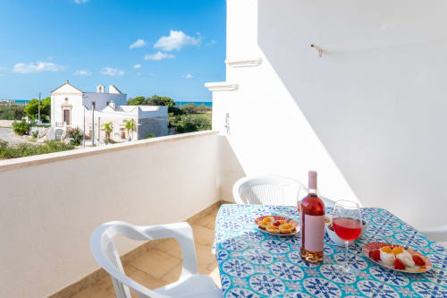 Balcone con tavolo preparato per vino rosé e stuzzichini, affacciato sulla cappella bianca e il Mar Adriatico a Villanova, Italia