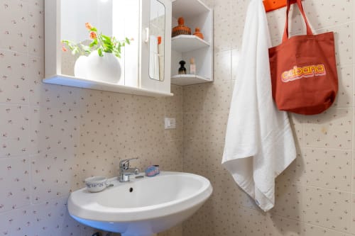 Bagno dell'appartamento Il Porticciolo con lavabo, specchiera, asciugamani bianchi e borsa rossa a Villanova, Italia