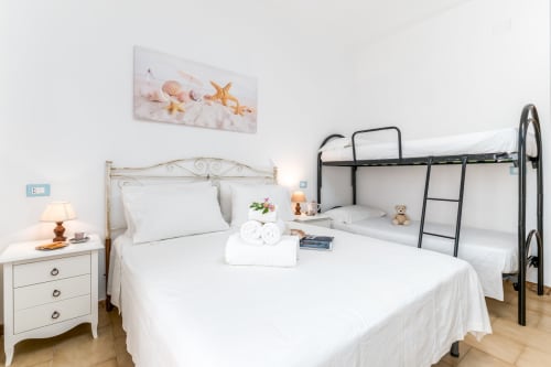 Camera luminosa con letto in ferro bianco, letto a castello, comodino in legno con lampada e quadri a tema marino a Il Porticicolo