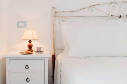 Camera da letto con letto a baldacchino in ferro battuto bianco, lampada da comodino e biancheria bianca presso la struttura vacanziale Il Porticicolo