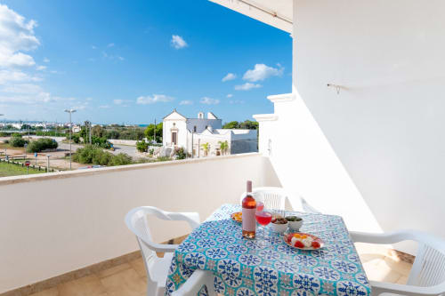 Terrazza di Il Porticciolo Vacanze a Villanova con tavolo da pranzo, vino e vista della cappella bianca sul paesaggio
