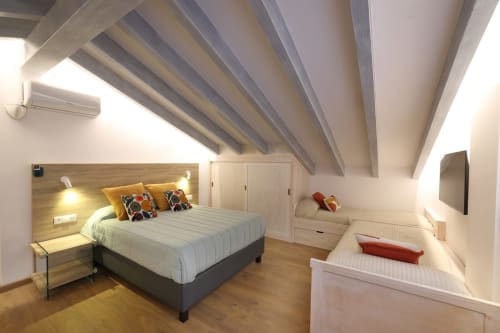 Luminoso dormitorio familiar en Torre de Quintana con vigas vistas, suelo de madera, cama de matrimonio con almohadas amarillas, empotrado