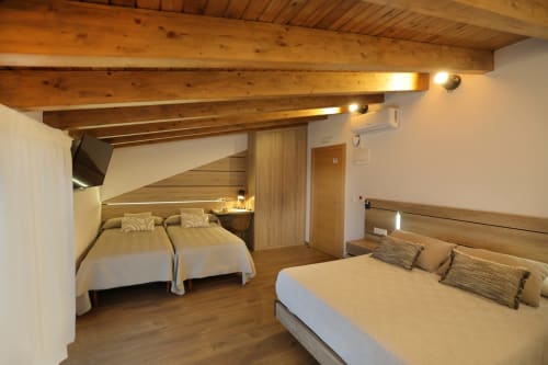 Habitación familiar del hotel Torre de Quintana en Suances con vigas de madera, dos camas individuales, cama de matrimonio y suelos de madera