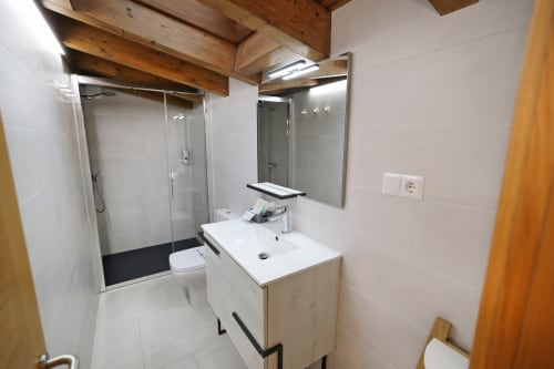 Baño moderno del hotel Torre de Quintana en Suances con lavabo blanco, espejo, ducha de cristal y viga de madera