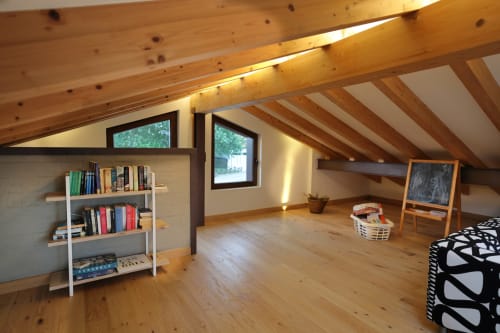 Luminosa habitación abuhardillada en Torre de Quintana, Suances, con vigas de madera vista, estantería y luz natural desde tragaluces.