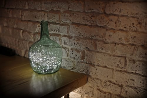 Botella de vidrio vintage con luces decorativas en repisa de madera frente a pared de ladrillo en el hotel Torre de Quintana, Suances
