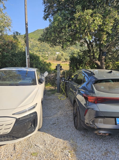 Zwei Elektrofahrzeuge laden am Hotel Les Mouettes in Belgodère, im Hintergrund Hügel und Bäume