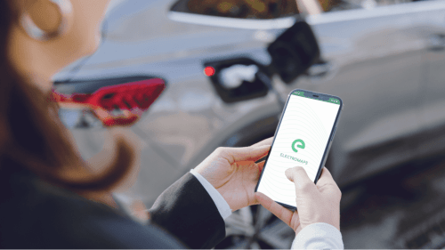 Person hält Smartphone mit ElectroMaps-App an einer Ladestation für Elektrofahrzeuge beim Hotel Les Mouettes, Belgodère