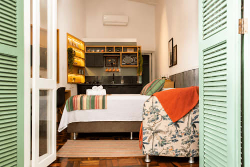 Aconchegante quarto de loft em Maringá com cama queen, detalhes em laranja, venezianas verdes, kitchenette e vista para jardim