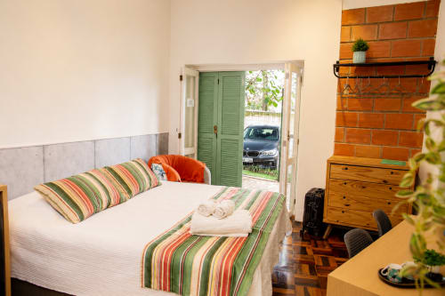 Quarto luminoso no CSS Maringá com cama estampada, lareira de tijolos e vista para o jardim através de portas francesas