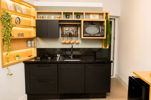 Cozinha moderna no Veneto Loft, Maringá com marcenaria preta, prateleiras amarelas, micro-ondas e iluminação ambiente