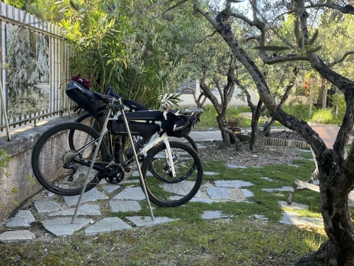 Vélo de touring noir et blanc garé sur un chemin de pierre à La Maison Gerval à Bédoin, entouré d'oliviers et d'un jardin luxuriant