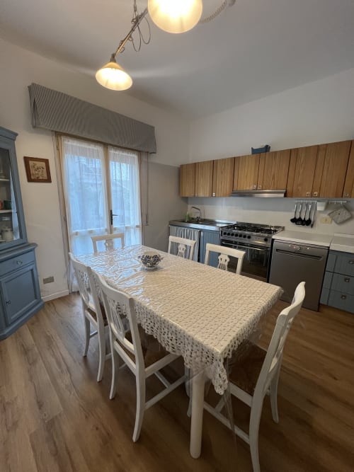 Sala da pranzo in stile vintage con sedie bianche, tovaglia color crema, elettrodomestici e vista sul giardino di Selva Marina Casa
