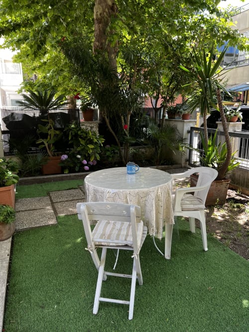 Area lounge esterna di Selva Marina Casa Vacanze a Riccione con tavolo rotondo, sedie bianche e lussureggiante vegetazione tropicale