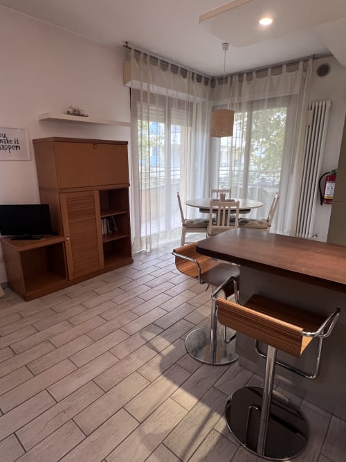 Zona living moderna con arredamento in legno, tavolo da pranzo e balcone con vista sul giardino a Selva Marina, Riccione