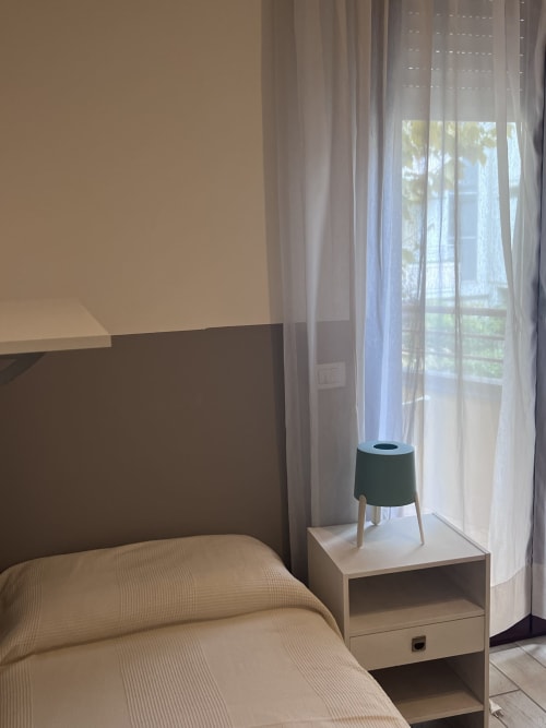 Camera moderna a Selva Marina Casa Vacanze a Riccione con vista sul giardino, comodino con lampada e tende trasparenti