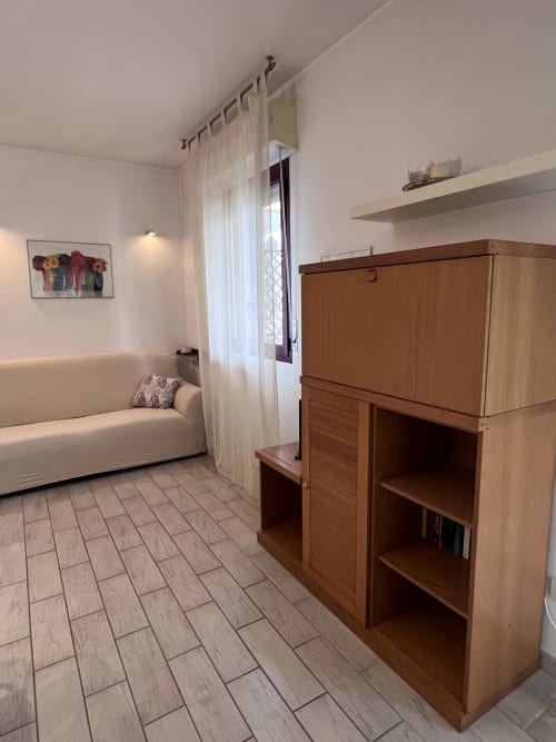 Soggiorno moderno con divano crema, mobile intrattenimento in legno con TV e vista sul giardino a Selva Marina Casa Vacanze