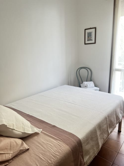 Camera da letto minimal a Selva Marina Casa Vacanze a Riccione con biancheria bianca, sedia in metallo e quadri
