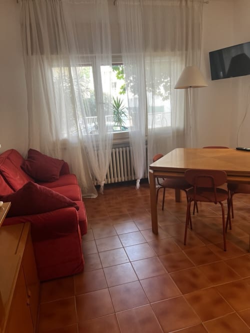 Luminoso soggiorno di Selva Marina Casa Vacanze a Riccione con divano rosso, tavolo da pranzo in legno e vista giardino