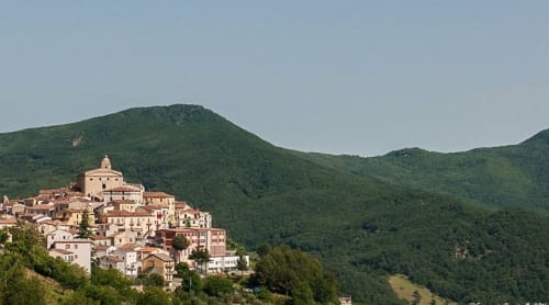 Il villaggio di Accettura arroccato sulla collina, con edifici in terracotta e una chiesa con cupola circondata da verdi montagne