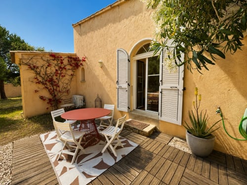 Terrasse ensoleillée de la villa Santa Reparata à L'Île-Rousse avec table rouge, chaises blanches et terrasse en bois dominant le jardin