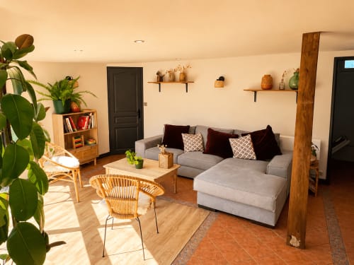 Séjour moderne du gîte Le Clos Divin avec canapé gris, mobilier en bois, plantes en pot et poutres apparentes