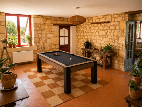 Salle de jeux rustique en pierre avec billard, carrelage damier, fenêtre à cadre rouge et plantes en pot au Clos Divin.
