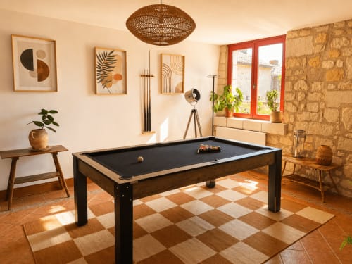 Élégante salle de jeux du gîte Le Clos Divin avec billard noir, poutres en bois, murs en pierre et décoration moderne