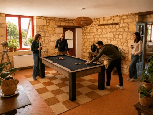 Cinq convives jouent au billard dans la salle de jeux rustique d'un cottage en pierre avec fenêtres à encadrements rouges au Clos Divin, Doué-la-Fontaine