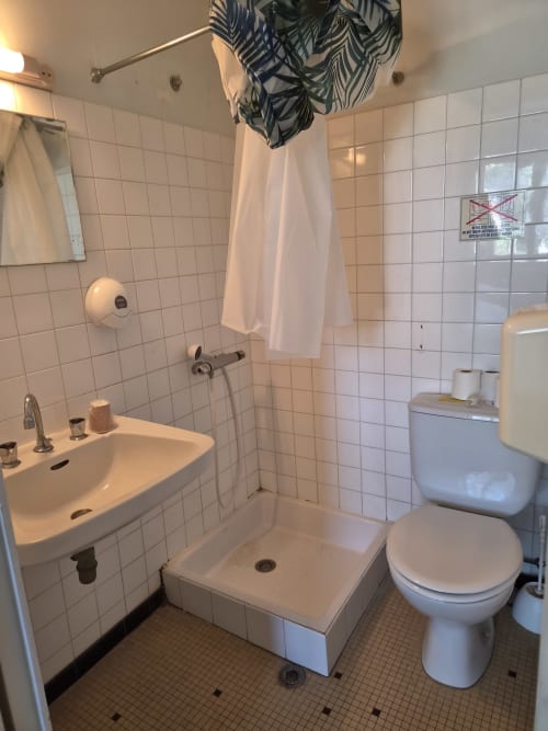 Salle de bain compacte carrelée de blanc avec lavabo, toilettes, douche et porte-serviettes à l'Hôtel Bar La Pinède, Saint-Jean-de-Monts