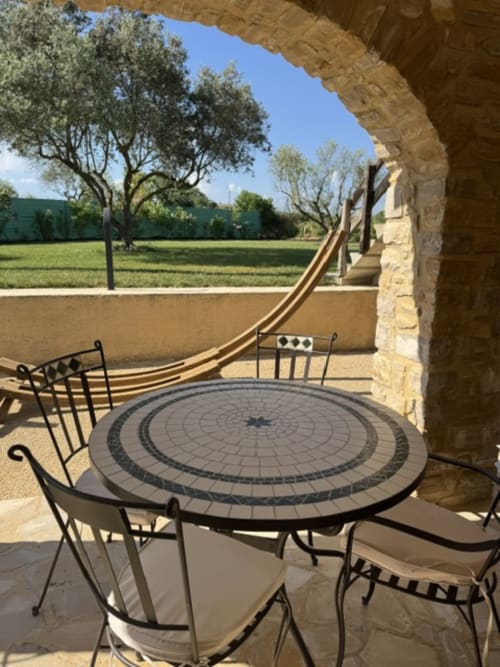 Schaduwrijk terras met ronde tafel en stoelen met uitzicht op olijfbomen en tuinen van L'arbre Qui Chante, Saint Sauveur de