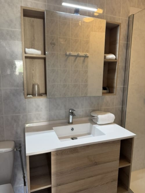 Moderne badkamer met witte wastafel, houten kasten en spiegel bij L'arbre Qui Chante B&B in Saint Sauveur de Cruzières