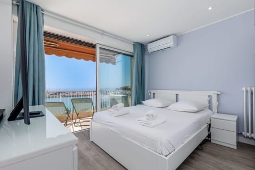 Chambre moderne et lumineuse à Riviera Home avec balcon vue mer, lit blanc et littoral méditerranéen visible