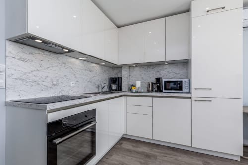 Cuisine blanche moderne avec comptoirs et dosseret en marbre, four intégré noir, électroménagers inox chez Riviera Home