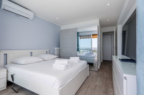 Chambre moderne à Riviera Home avec balcon vue mer, lit blanc, TV et climatisation à Roquebrune-Cap Martin