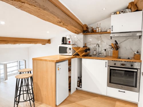 Cuisine moderne de l'appartement Le Petit Rochelois à La Rochelle, avec poutres en bois, armoires blanches, four inox et bar