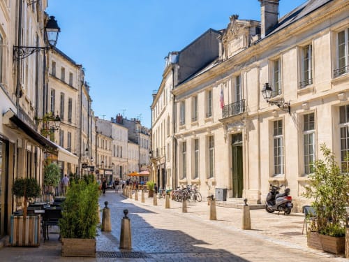 Charmante rue pavée à La Rochelle avec bâtiments historiques beige, idéale pour les hôtes de l'appartement ARLOÉ