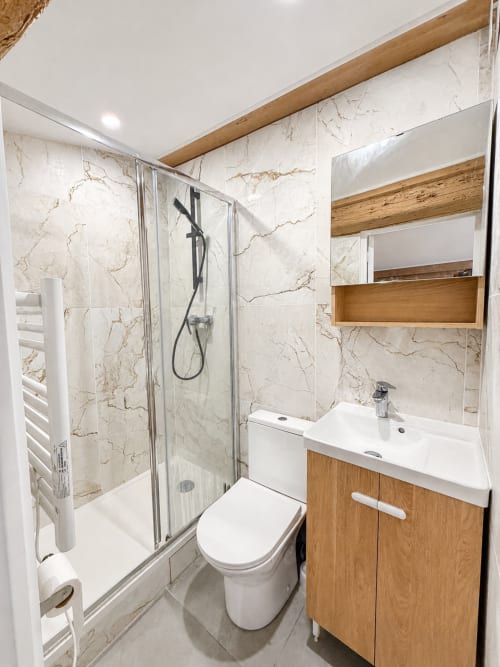 Salle de bain moderne de l'appartement ARLOÉ avec murs en marbre, meuble vasque en bois, douche et porte-serviettes à La Rochelle
