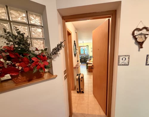 Accogliente ingresso dell'appartamento CaseCasadei a Rocca Pietore con stelle di Natale rosse, porta in legno e pavimento in cotto