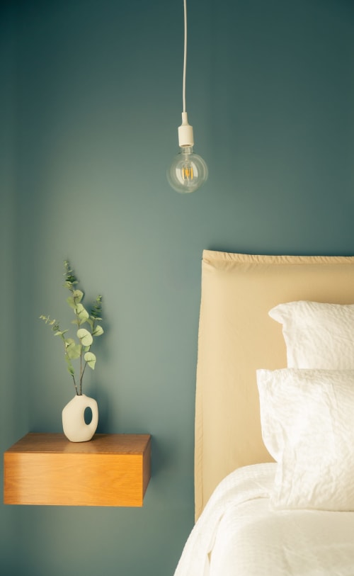 Chambre de La Maison du Potier à Valras-Plage avec murs bleu-vert, luminaire suspendu, table de nuit en bois, linge blanc et