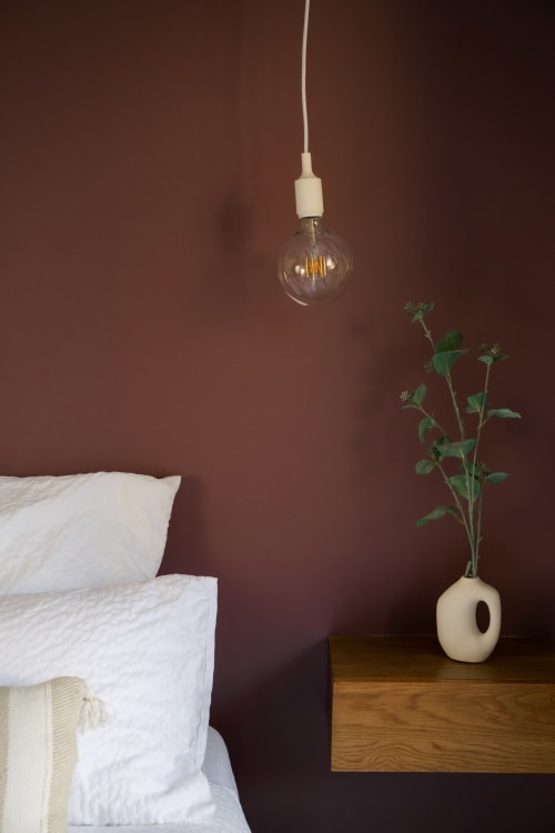 Minimalist bedroom at La Maison du Potier B&B in Valras-Plage with burgundy walls, white bedding, pendant light, and plant