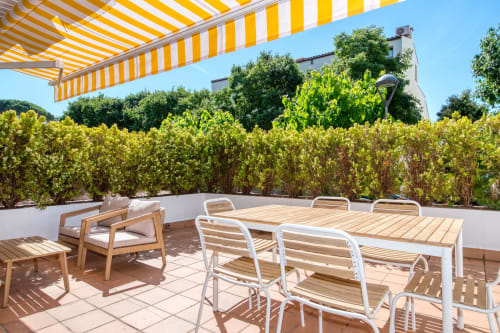 Sunny terrace at Niu d'Or apartment in Palafrugell with dining furniture, yellow striped awning, and lush garden views