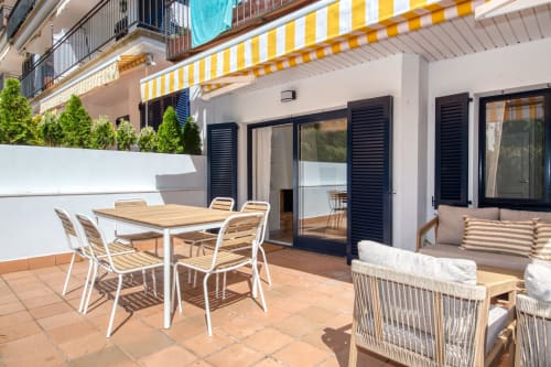 Sunny terrace at Niu d'Or apartment in Palafrugell with dining table, lounge chairs, striped awning, and private patio