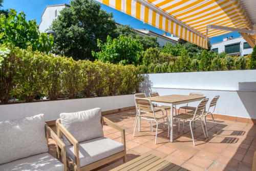 Sunny private patio at Niu d'Or apartment in Palafrugell with dining table, lounge chairs, and lush garden views