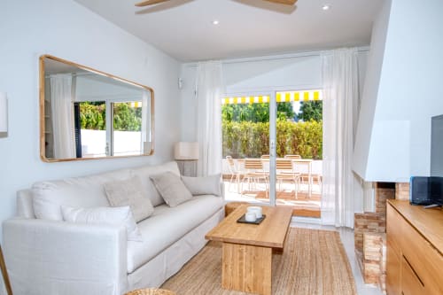 Bright living room with white sofa, wooden furniture, garden view doors opening to patio at Niu d'Or apartment in Palafrugell