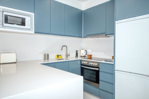 Modern blue and white kitchen in Palafrugell apartment with stainless steel appliances and white countertops
