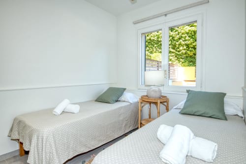 Twin bedroom with green pillows in Niu d'Or apartment, Palafrugell, overlooking garden through glass doors