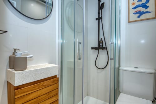 Modern bathroom with walk-in shower, wooden vanity, and round mirror at Niu d'Or apartment in Palafrugell