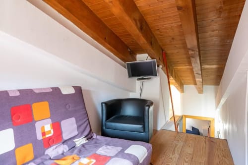 Dormitorio moderno de apartamento en Montgat con cama púrpura, sillón negro, TV de pantalla plana, vigas de madera y vistas a las montañas