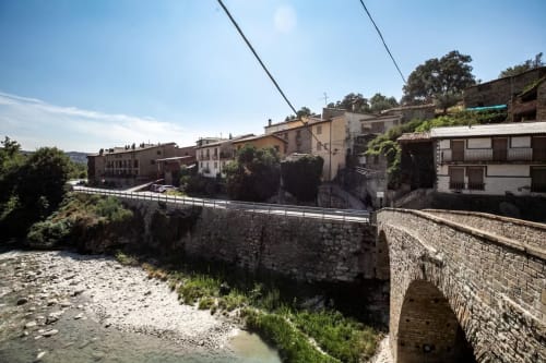 Puente de piedra sobre río con edificios tradicionales en Montgat, pueblo de montaña en los Pirineos